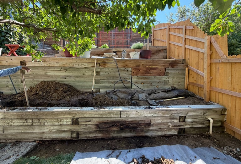 Rustic wooden raised garden beds in a backyard with compost, wood fence, and potted plants in background