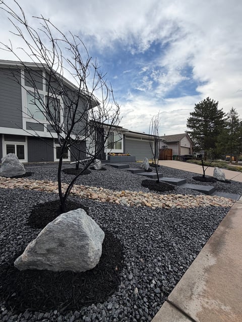 Modern home exterior with gravel landscaping, bare tree, and large rocks