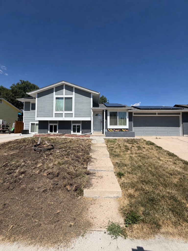 Modern white two-story home with solar panels, garage, and concrete driveway on a mostly bare lot under clear blue sky