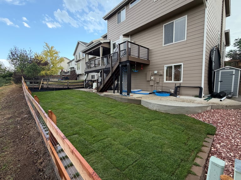 Two-story beige house with deck overlooking a green lawn and backyard patio area
